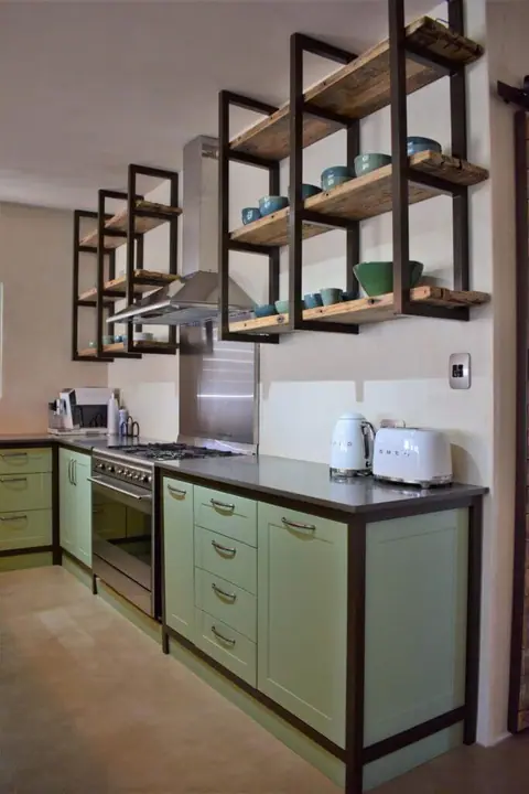 Fully equipped kitchen with sage-green cabinets and open shelving